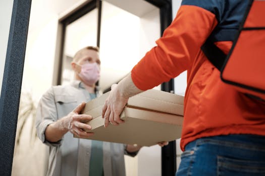 Home A deliveryman hands over pizza boxes while wearing a mask, highlighting contactless delivery during the pandemic.